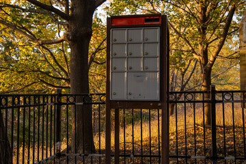 Autumnal scene with mailbox units - golden hour lighting casts warm tones on foliage - wrought iron fence frames composition - tranquil suburban atmosphere. Taken in Toronto, Canada.
