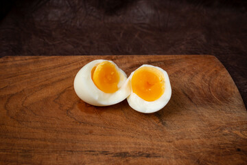Ripped in half boiled free range egg isolated on a wooden chopping board and dark background