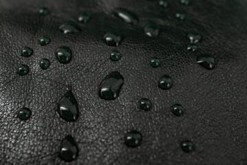Round water drops on black leather texture, side view, soft focus macro pattern