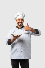 Indian asian young Chef in uniform happily presenting empty white ceramic plate on white background