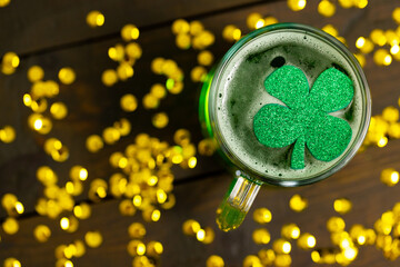 Image of beer glass, clover and gold confetti on wooden background © vectorfusionart