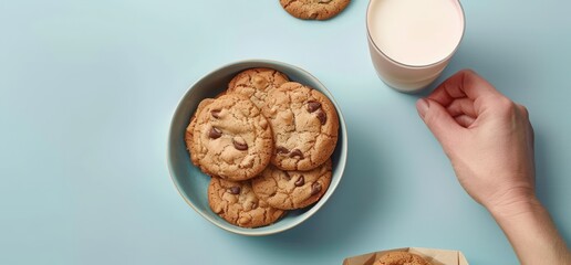 grinding cookies with milk on a light blue background for World Chocolate Chip Cookie Day, a hand holding a glass of white cream and a paper cup filled with food