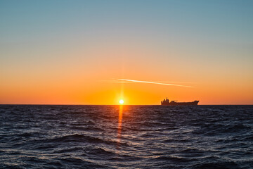 Fototapeta premium Beautiful ocean sunrise, with colourful sky, dark sea and silhouette of ship on the horizon.