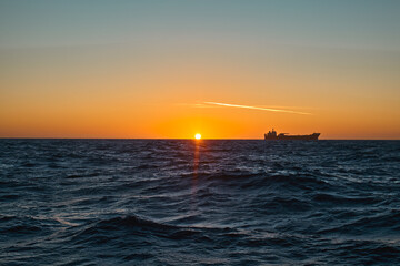 Ocean sunrise, with colourful orange sky, dark sea and silhouette of ship on the horizon.