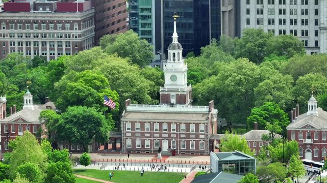 Historic Independence Hall in Philadelphia. Downtown Philly city theme. Aerial establishing shot with American flag and green trees.