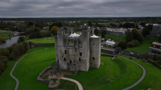 Trim Castle, County Meath, Ireland, October 2023. Drone orbits counter clockwise and pulls backwards ascending to an elevated view of the Medieval Fortress surrounded by greenery on cloudy day.