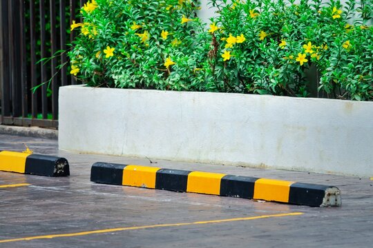 A yellow and black striped curb is in front of a white wall. The curb is empty and there are no cars parked in the lot
