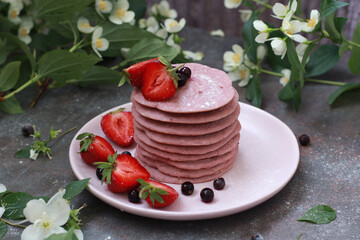 Delicious breakfast setting with a stack of homemade berry pancakes topped with fresh strawberries and cream. The vibrant colors and flowers create an appetizing and inviting summer morning scene