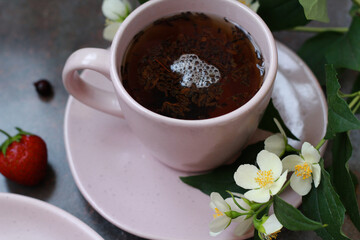 An elegant pink cup filled with aromatic tea, surrounded by jasmine flowers and fresh berries of strawberry and blackcurrant, creates an atmosphere of morning coziness and tranquility.