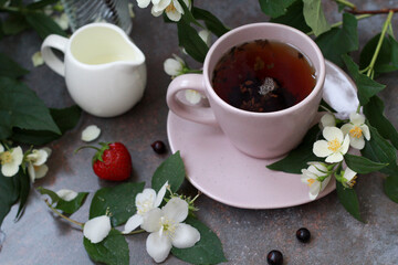 An elegant pink cup filled with aromatic tea, surrounded by jasmine flowers and fresh berries of strawberry and blackcurrant, creates an atmosphere of morning coziness and tranquility.