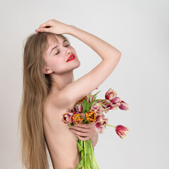 Happiness lady with eyes closed holding spring flowers in one hand and covering chest with flowers
