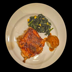 Chicken steak, mashed potatoes and spinach on a white plate. Isolated on black background.