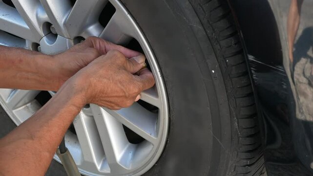 close up to car's tire while driver inflating car tire in sunny daytime. Hand holding hose with air pressure gauge and filling up car's tire with nitrogen air.mechanic checking tire pressure.