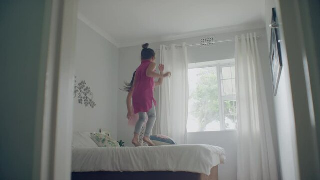 Two sisters playing in the their room and jumping on the bed