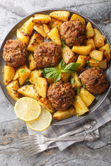 Bifteki is a Greek burger juicy and flavorful biftekia baked with crispy potatoes in a lemon olive oil sauce closeup on the plate on the table. Vertical top view from above