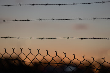 Barbed wire fence silhouetted against a sunset sky