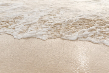 Bubbly white ocean sea foam washing up over a white sand beach.
