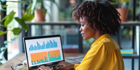 An African American woman reviewing financial information on a laptop in a blended office environment for a digital entrepreneurship performance tracking system.