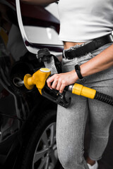 Fototapeta premium A woman fills a car with fuel at a gas station. Gas station service. Refueling concept. 