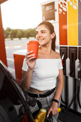 A woman fills a car with fuel at a gas station. Gas station service. Refueling concept. 