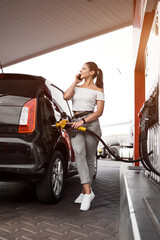 A woman fills a car with fuel at a gas station. Gas station service. Refueling concept. 