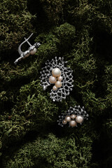 Silver brooch and earrings with pearls on a background of green moss. Top view. 