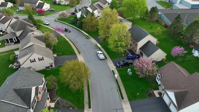 Quaint American neighborhood at sunset. Two story middle class homes with blossoming spring trees. Car on street. Solar panels on roof producing green eco-friendly energy. Aerial top down flyover.