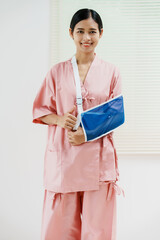 A young Asian female wearing a pink patient uniform stands isolated against a white wall...