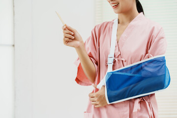 A young Asian female wearing a pink patient uniform stands isolated against a white wall...