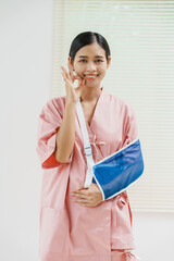 A young Asian female wearing a pink patient uniform stands isolated against a white wall...