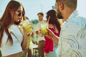 Friends, man and woman clink their glasses in festive toast, their faces lit up with smiles and sun's glow at evening party. Concept of party, Friday mood, celebration, summer holidays, relax.