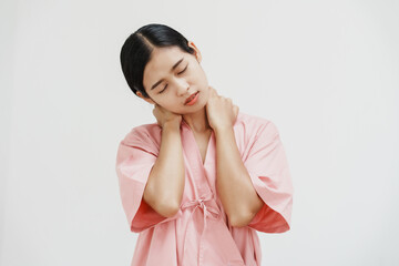 A young Asian female wearing a pink patient uniform stands isolated against a white wall...
