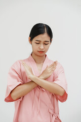 A young Asian female wearing a pink patient uniform stands isolated against a white wall...