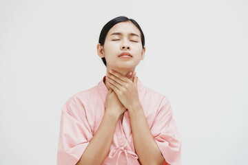 A young Asian female wearing a pink patient uniform stands isolated against a white wall...