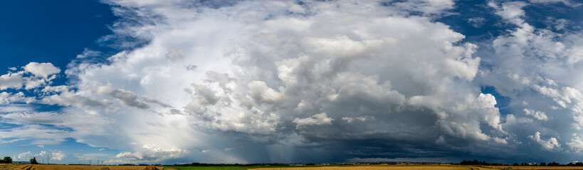 Obraz premium Panoramaaufnahme der weiß-grauen, stark in Bewegung befindlichen Wolkenmassen einer übers Land ziehenden Gewitter- oder Superzelle am Horizont