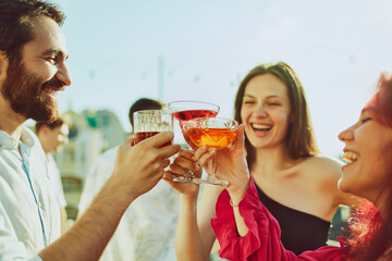 Group portrait of young adults gathers for festive toast, on party and their drinks glowing in radiant sunlight. Concept of party, Friday mood, celebration, summer holidays, relax.