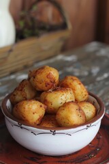 A bowl of crispy roasted potatoes is set on a rustic table, showcasing their golden-brown texture and seasoning. The potatoes are beautifully roasted, with a crunchy exterior and tender interior, maki
