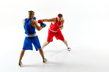 Dynamic scene of two athletes, one in red and one in blue, training their fighting techniques against white studio background. Concept of professional combat sport, healthy lifestyle, competition. Ad