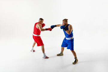 Two determined boxers in blue and red attire in action refining their techniques during intense training session against white studio background. Concept of professional sport, competition. Ad