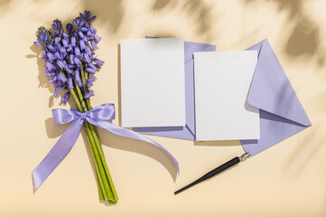 A bouquet of lavender spring scilla, two lilac envelopes and blank cards on a beige background. Mockup greeting card, invitation.Copy space.