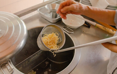 Cooking person in the restaurant is cooking while using a sieve for scalding yellow noodles in a silver pot.Sieve boiled noodles yellow.