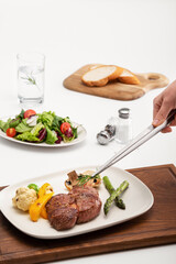 스테이크, 샐러드, 바게트가 있는 식탁에서 조리용 핀셋으로 마지막 플레이팅을 하고있다.
