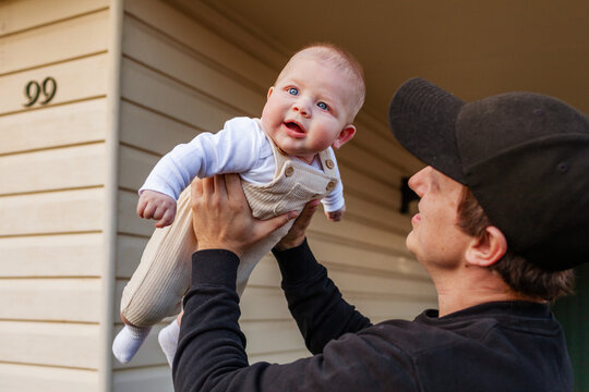 Young dad holding his baby son up in the air outside family home - Powered by Adobe