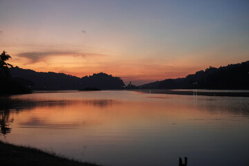 Obraz premium A beautiful sunset over Sermo lake, Yogyakarta, with a small island in the middle. The sky is a mix of pink and purple hues, creating a serene and peaceful atmosphere.