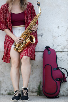 Unrecognizable young woman with saxophone against urban wall