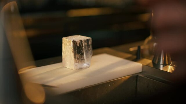 on the bar counter on white board there is a square cut transparent ice for whiskey
