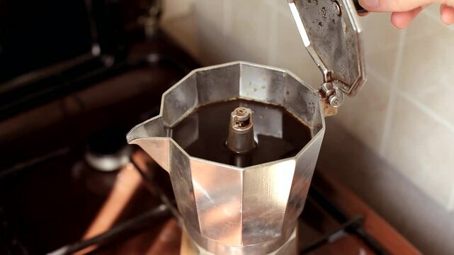 A hand opens a coffee maker filled with hot strong coffee.