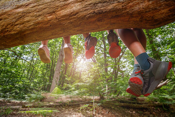 Feet of happy kids dangle off a log above green summer forest
