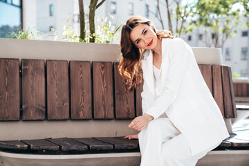 Young beautiful brunette woman wearing nice trendy white suit jacket. Sexy smiling model posing in the street at sunny day. Fashionable female. Cheerful and happy. Evening makeup, red lips