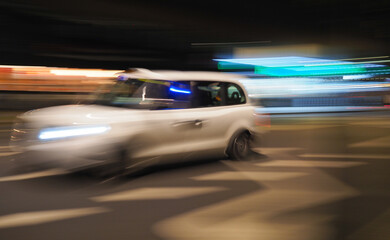 Semi-abstract picture of a white taxi at night with motion blur and neon light background
